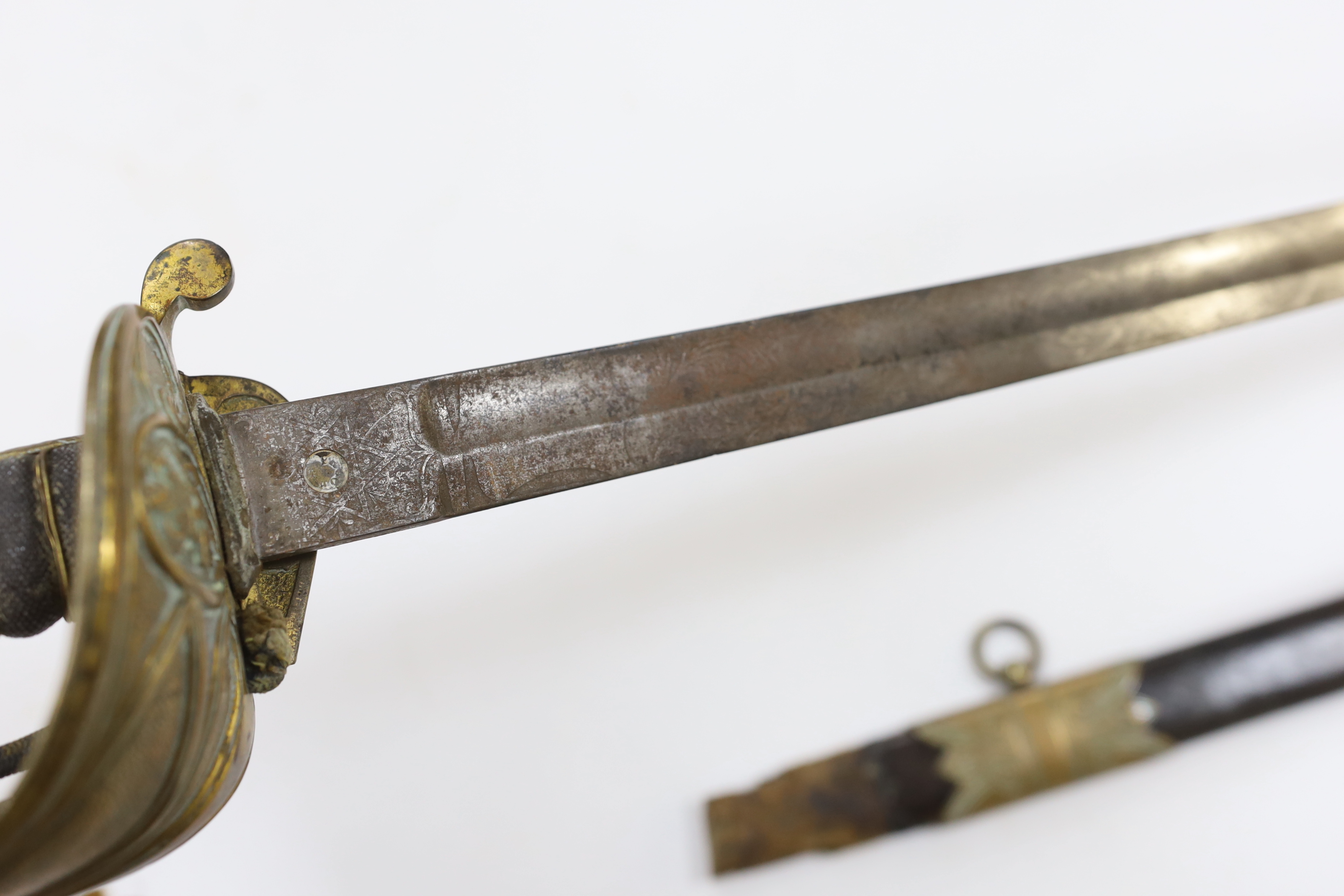 A late Victorian naval officer’s sword with regulation brass hilt, lion head pommel and blade etched with crown, VR and fouled anchor in its leather scabbard, top mount missing, blade 77cm